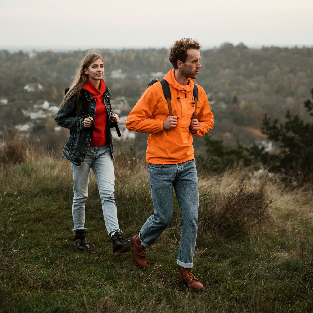 Two people hiking in a scenic outdoor setting with a forest in the background.