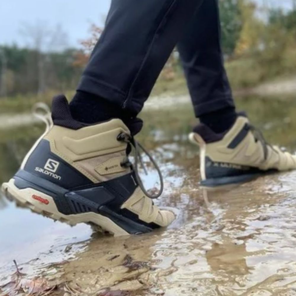 Person wearing Salomon boots walking through a shallow stream.