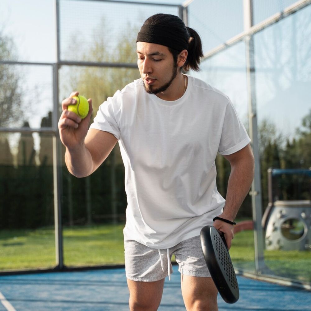Person holding a tennis ball and paddle on a tennis court